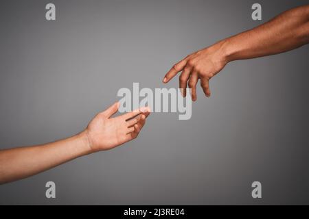 Get in touch with your classical side. Studio shot of unidentifiable hands reaching for each other against a gray background. Stock Photo