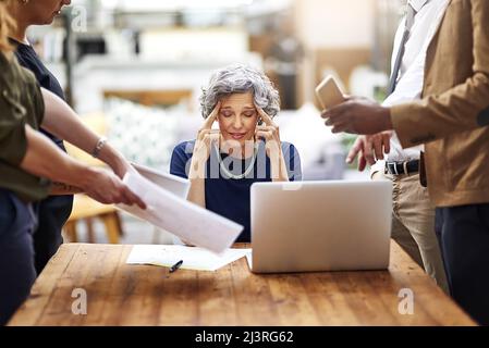 Strained by so many difficulties. Cropped shot of a stressed out businesswoman surrounded by colleagues needing help in an office. Stock Photo