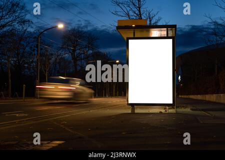 Blank advertisement board as a mock-up template in the city. Empty screen at a bus stop during the night. A car driver is passing by very fast. Stock Photo