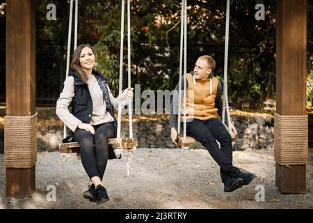 A young man with his lover are sitting on a swing in the forest among the trees. High quality photo Stock Photo