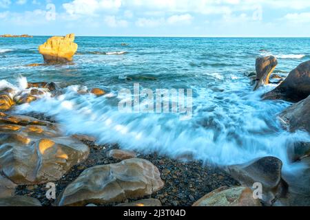 Waves crashing on the shore creating silk-like streaks of different shapes piercing the rock at the beach in the afternoon is beautiful and relaxing Stock Photo