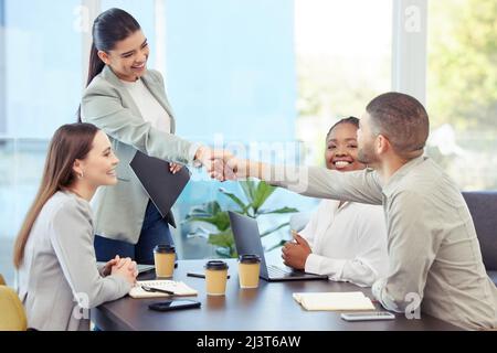 The strength of the team is each individual member. Shot of two colleagues shaking hands while in a meeting with colleagues in a boardroom. Stock Photo