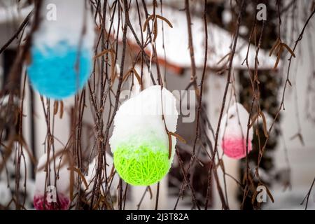 Snow-covered woolen ornaments hang on tree branches close-up. Stock Photo