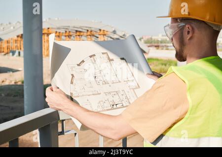 Construction engineer wearing safety vest and work helmet standing at construction site and working on apartment building project Stock Photo