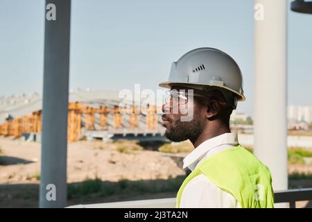 Contemplative modern constructor in safety vest and hardhat working on new house Stock Photo