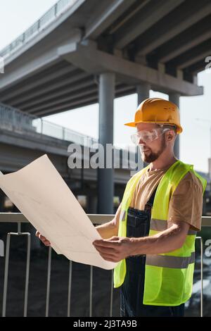 Building worker analyzing project plan and standing on construction site without walls Stock Photo