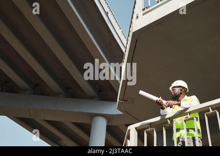 Construction engineers wearing safety vests and work helmets standing at construction site and working on apartment building project Stock Photo