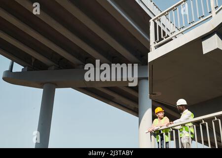 Professional engineers in workwear standing at construction site and discussing building process Stock Photo