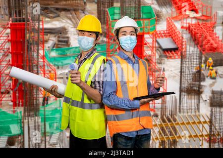 Two young asian engineers wearing surgical mask with tablet and blueprint New normal concept. (With clipping path) Stock Photo