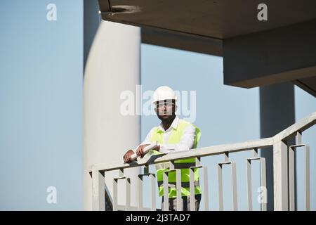 Engineers in protective vests and hardhats analyzing online sketch on tablet while planning work at construction site Stock Photo