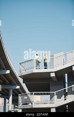Large construction project in city: busy engineers working with blueprint and standing on construction site of skyscraper without walls Stock Photo
