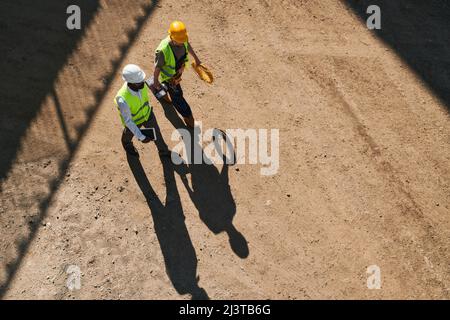 Contemplative modern constructors in safety vests and hardhats working on new house and discussing building process Stock Photo
