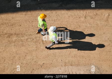 Construction workers examining blueprint and standing on building site of apartment house, large block of flats under construction Stock Photo