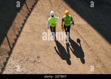 Directly above view of professional engineers in workwear standing at construction site and discussing building process Stock Photo
