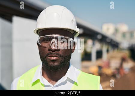 Serious handsome mixed race construction foreman in glasses standing at construction site Stock Photo