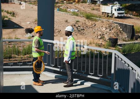 Two construction workers wearing hardhats and chatting while standing against sky in background, copy space Stock Photo
