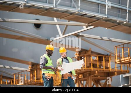 Two construction workers wearing hardhats while chatting at construction site, copy space Stock Photo
