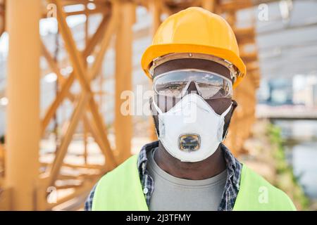 Serious pensive construction workers in green waistcoats and work helmets standing on site and discussing location of modern building in city Stock Photo