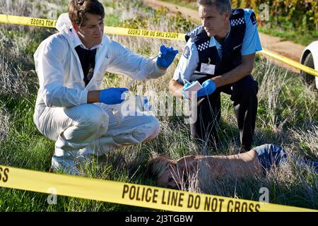 Examining the evidence. Shot of two investigators examining evidence at a crime scene. Stock Photo