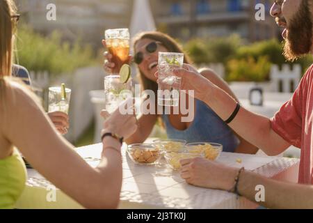 Happy hour toasting. Young friends clinking with fresh mojitos sitting in a counter restaurant and taking aperitif in the summer. Friendship and toget Stock Photo