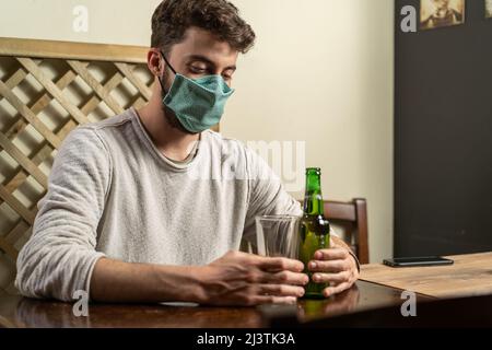 Guy with fashion face mask drinking beer alone in a indoor pub. new normal concept of young people new behaviors during corona virus (Covid-19) pandem Stock Photo