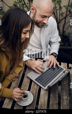 Couple of young people surfing the web sitting at outdoors cafe using a laptop computer Stock Photo
