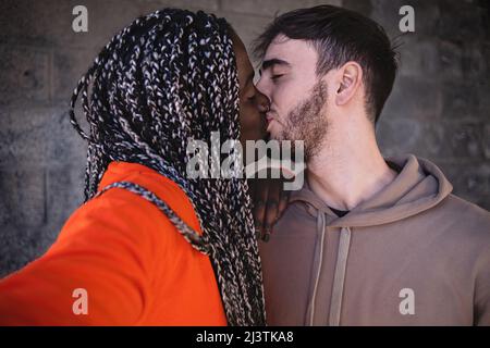 Engaged multiethnic couple of young people taking a selfie during a kiss - biracial sweethearts hugging and taking romantic moments Stock Photo