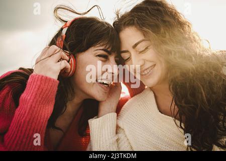 Tender couple of young girlfriends carefree outdoors listening and sharing music from headphones Stock Photo