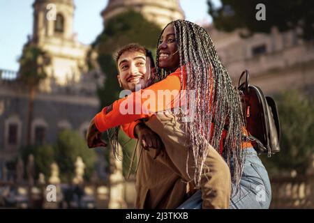 Cheerful couple of millenial travelers turning in the baroque city center piggybacking against a church background - International urban tourism in th Stock Photo
