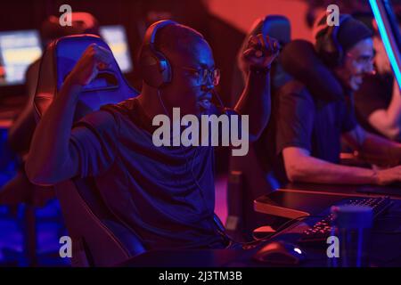 Positive young Black guy in headphones gesturing hands like monkey while winning game, he participating in esports championship Stock Photo