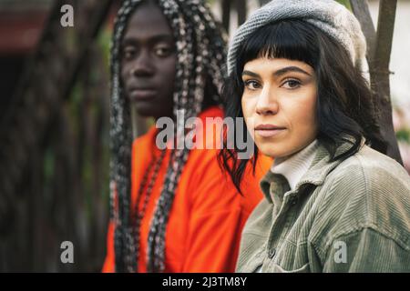 Portrait of two 20-year-old girls of different races while, sitting outdoors, looking at the camera -. friendship and integration concept Stock Photo