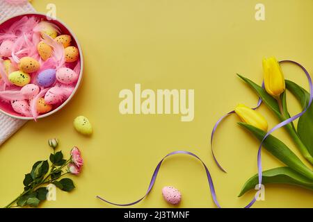 Easter bright background. Pink bowl with colorful eggs, pink feathers, spring flowers. Happy Easter concept. Post card with copy space. Stock Photo