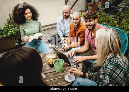 Multicultural university students using laptop around a table in the hostel rooftop. Students working together on academic project finding information Stock Photo