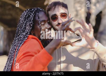 A couple of young multiracial young people make the heart shape with their fingers - Diverse people loving each other concept Stock Photo