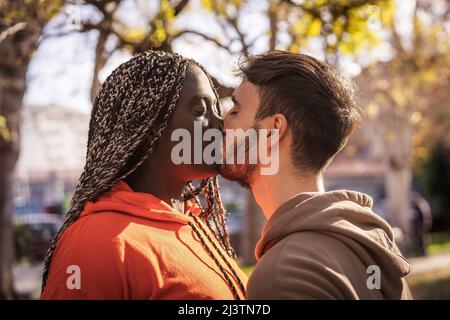 A young couple of people of different ethnicities kissing outdoors. Stock Photo
