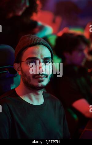 Portrait of content young Arabian gamer in eyeglasses participating in esports league, neon light Stock Photo