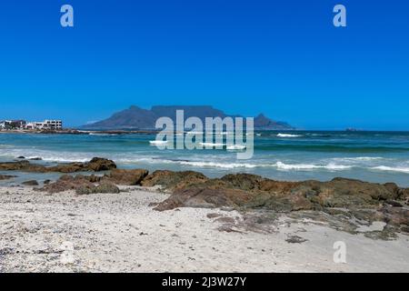 Beach, rocks and ocean with Table Mountain in the background. Against a clear blue sky. Stock Photo