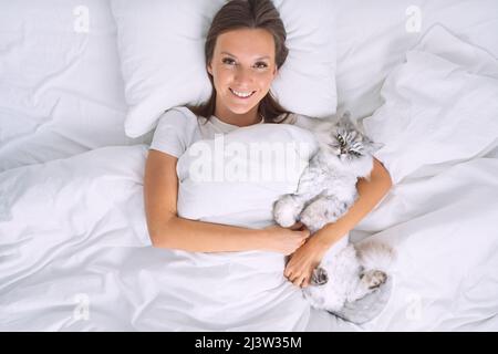 Beautiful woman lying on the bed and hugging her lovely cute cat. Sleeping with cat Stock Photo