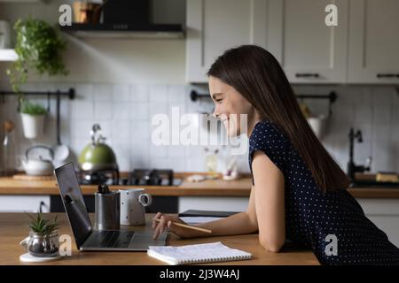 Woman studying on laptop standing lean at kitchen table Stock Photo