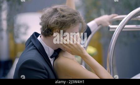 Stylish happy wedding couple softly hugging indoors during photosession. Action. Side view of romantic newlywed groom and bride. Stock Photo