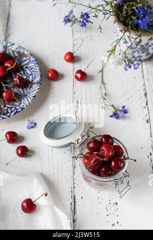 Fresh sweet cherries on plate and jar on white wooden table with blue flowers Stock Photo