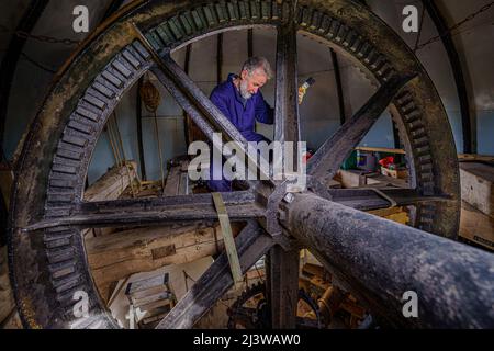 Volunteers clean and grease cogs inside Wilton windmill, Wiltshire, where members of the Wilton Windmill Society are helping to complete the annual Spring clean of the traditional tower mill with fantail, built in 1871 and operational for 100 years. Picture date: Sunday April 10, 2022. Stock Photo
