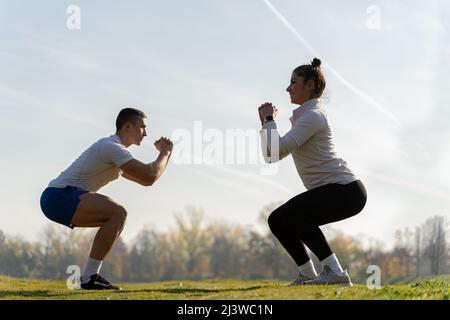 Two amazing and attractive fit friends are doing squad exercise on the grass Stock Photo