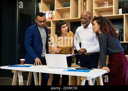 Exploring new ventures with technological assistance. Shot of a group of creative businesspeople discussing something on a laptop. Stock Photo