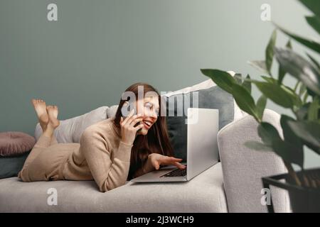 Beautiful woman speaking on mobile phone while using laptop for remote work. Online shoping Stock Photo
