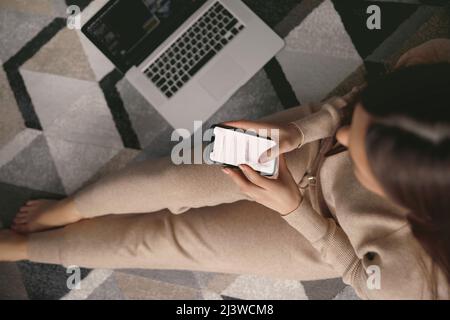 Woman holding credit card and using phone sitting on floor. Payment.  Online shopping Top view Stock Photo
