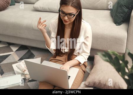 Young woman sitting on the floor and using laptop for remote work. Stock Photo