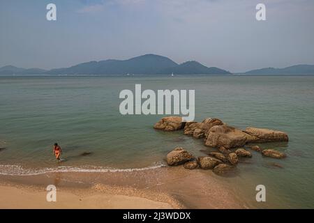 The view of beach with rocks and a lady, during morning at Damai Laut Beach in Lumut, Malaysia. Stock Photo