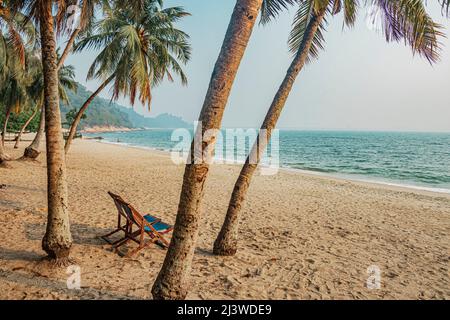 An empty chair on sandy beach between the coconut trees at Teluk Batik Beach near Lumut in Perak, Malaysia. Stock Photo