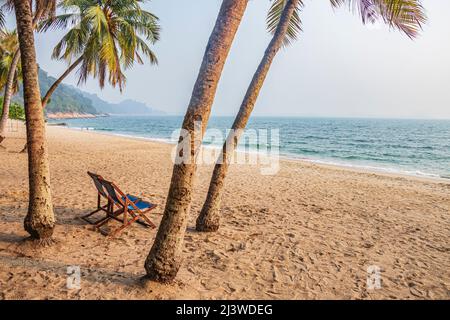 An empty chair on sandy beach between the coconut trees at Teluk Batik Beach near Lumut in Perak, Malaysia. Stock Photo